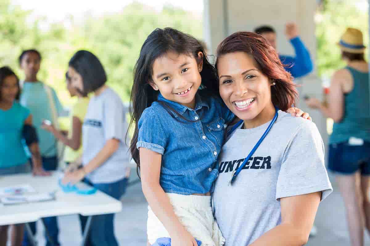 an adult holding a child and wearing a volunteer tshirt, both smiling at the camera