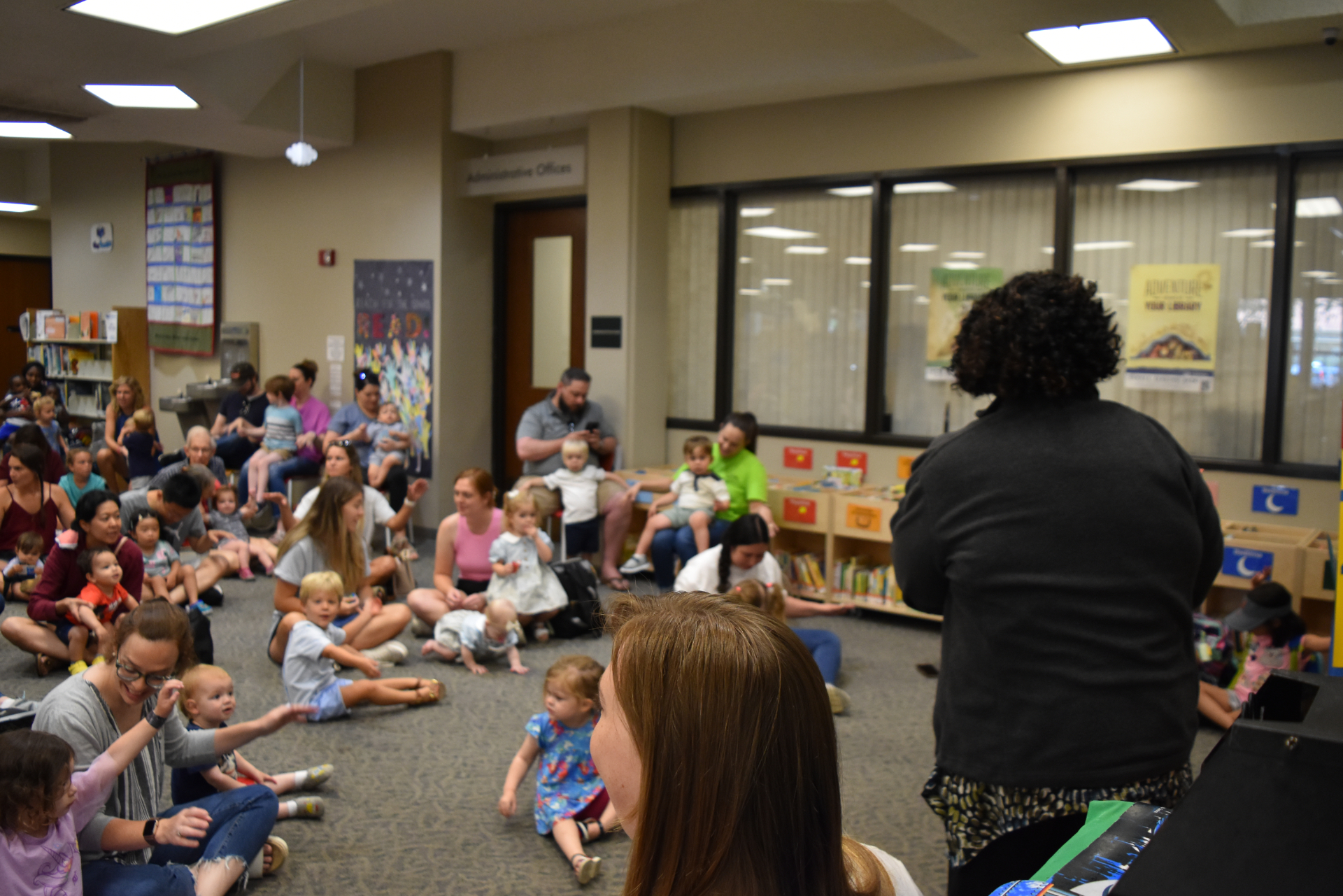 children and adults sitting on the floor while a library staff member stands in front of the group