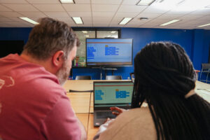 Two individuals looking at a laptop that is also projecting its image on a larger TV screen