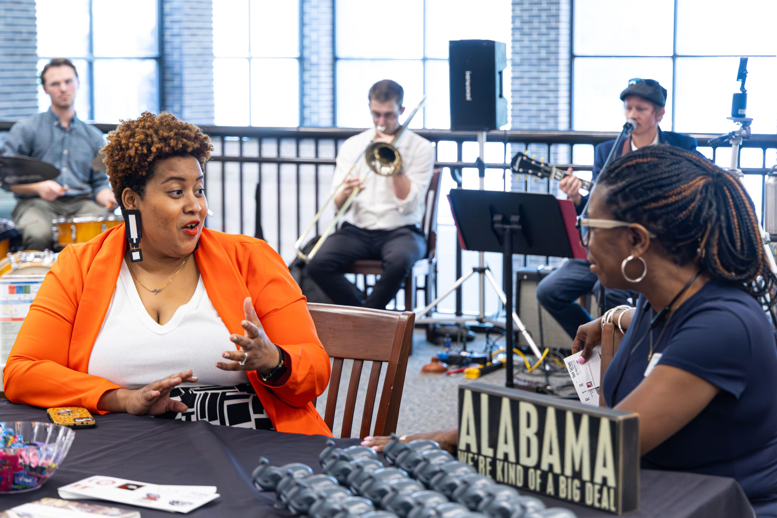 Two women seated and talking with musicians playing in the background